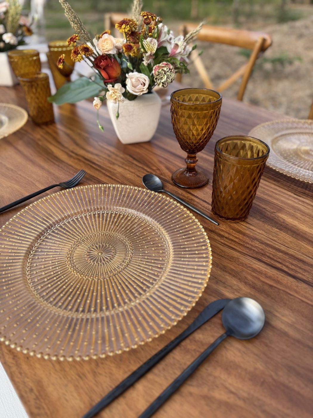 Gold relief glass charger: Set with black cutlery and amber glassware on a guanacaste table