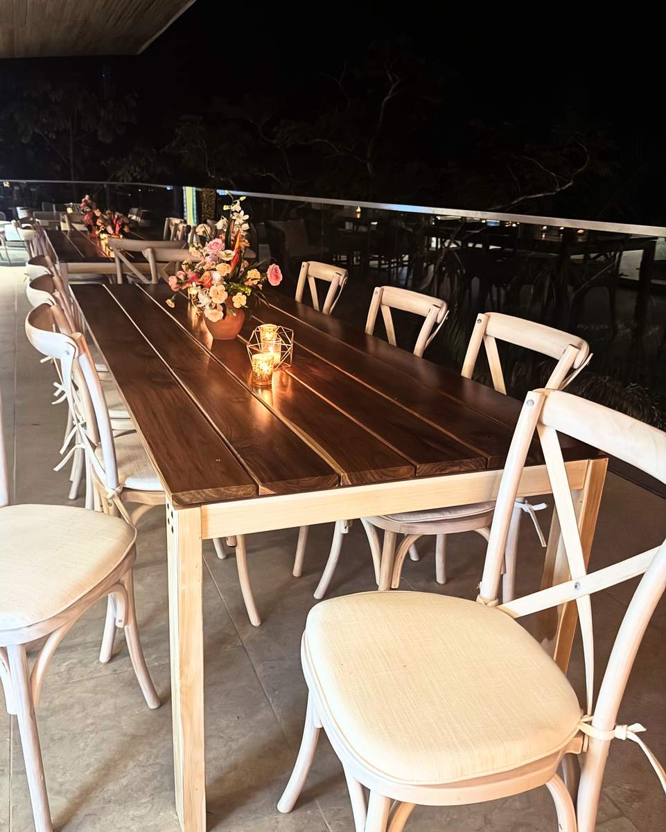 Teak tables with white crossback chairs, candles and tropical flowers at an evening dinner