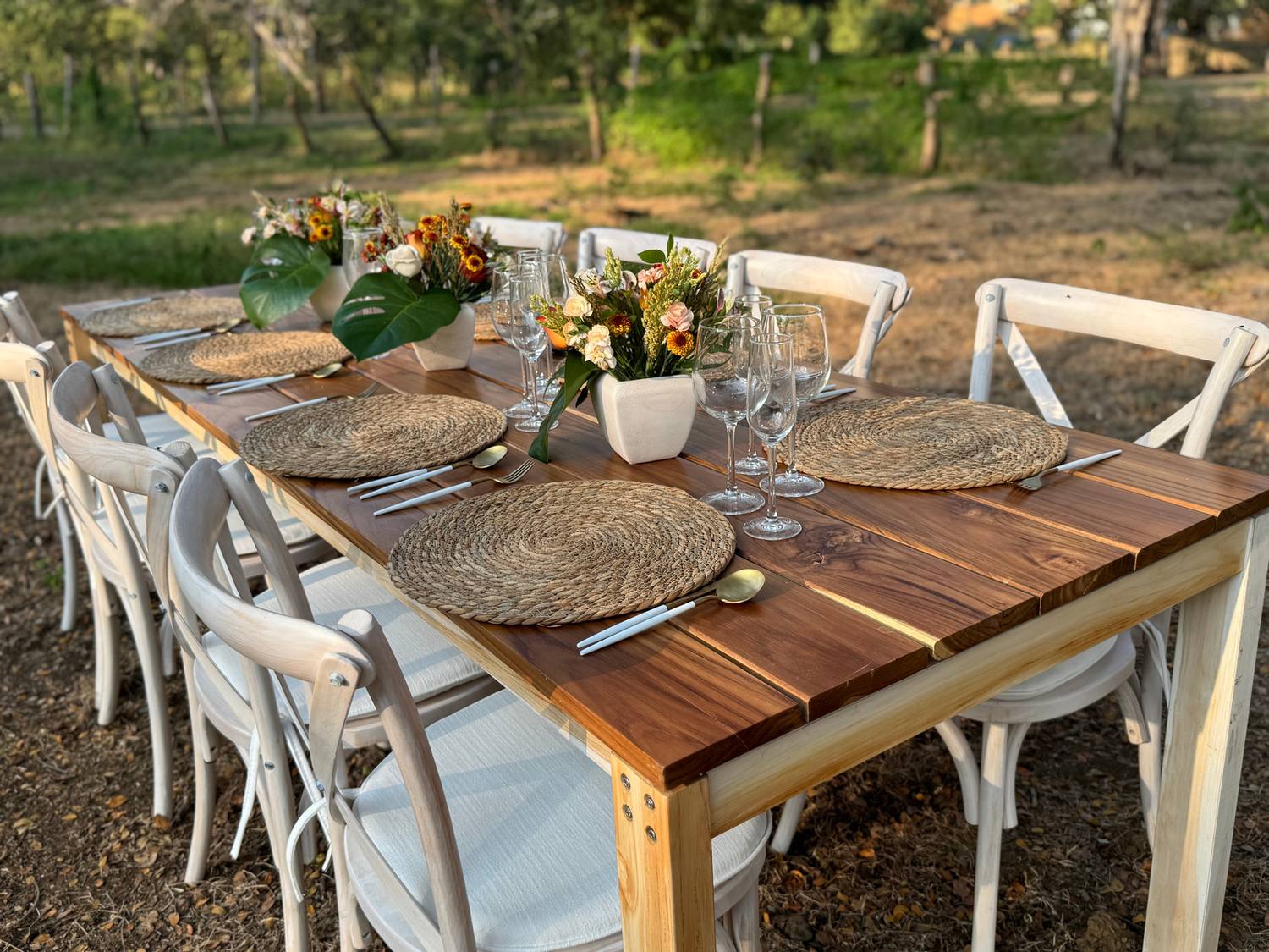 Teak table set for dinner with white crossback chairs, wicker chargers and flowers