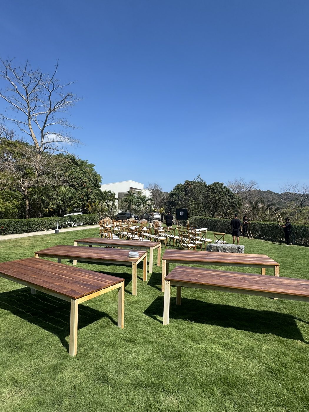 Teak table: Teak tables set out on a lawn before a villa wedding